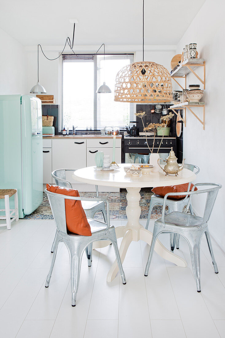 Metal chairs around a baluster table in the kitchen-living room with a white floor