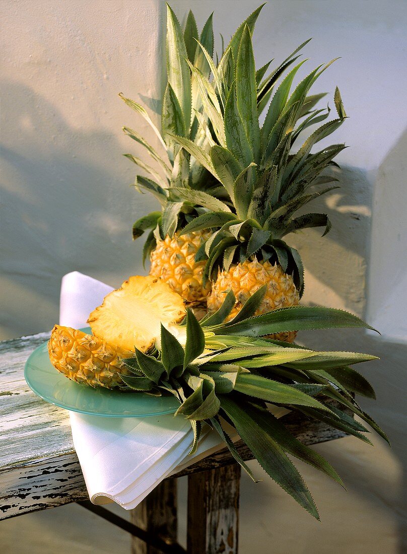 Drei Ananas, davon eine halbiert auf Teller, auf Holztisch