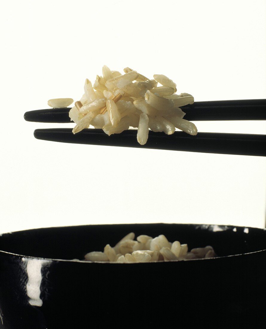 Reis auf schwarzen Stäbchen über einer Schale Reis