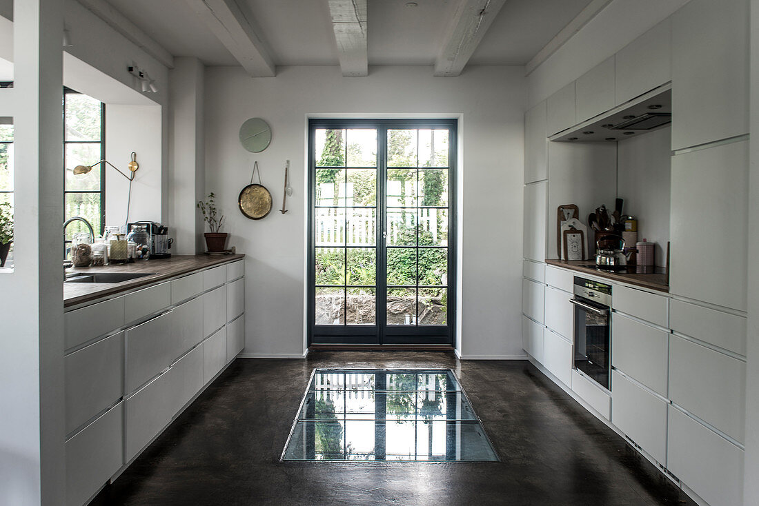 White built-in cabinets in front of window and floor with glass insert in front of French doors in kitchen