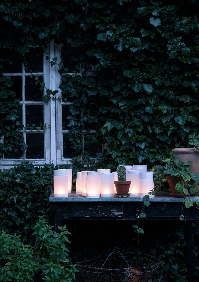 White paper lanterns on an old table in front of the summer house with ivy