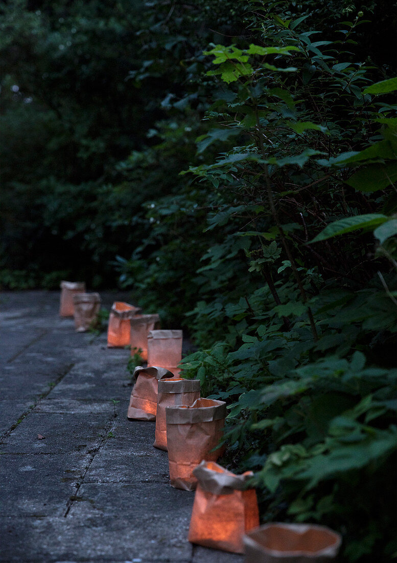 Windlichter in braunen Papiertüten am Weg im abendlichen Sommergarten