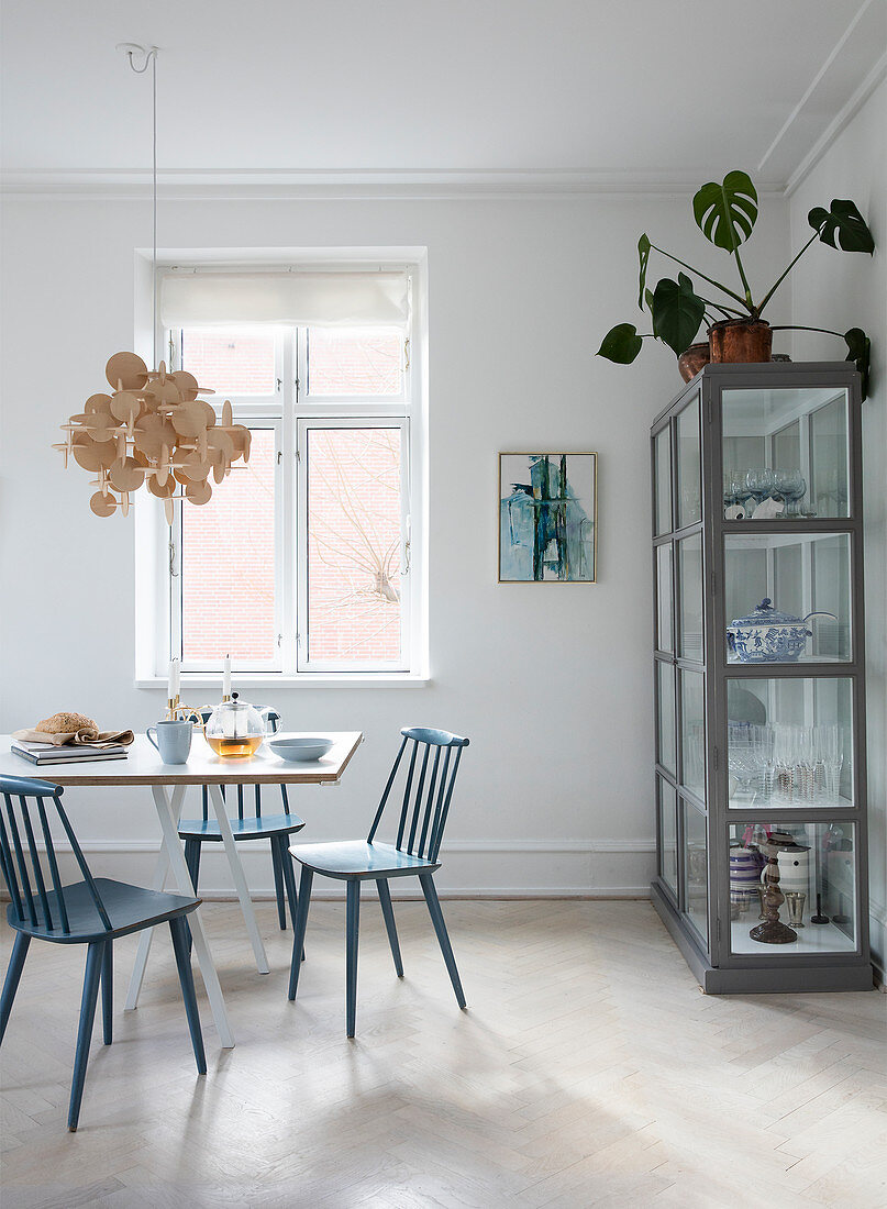 Blue spoke-back chairs at a dining table in front of a glass cabinet filled with crockery