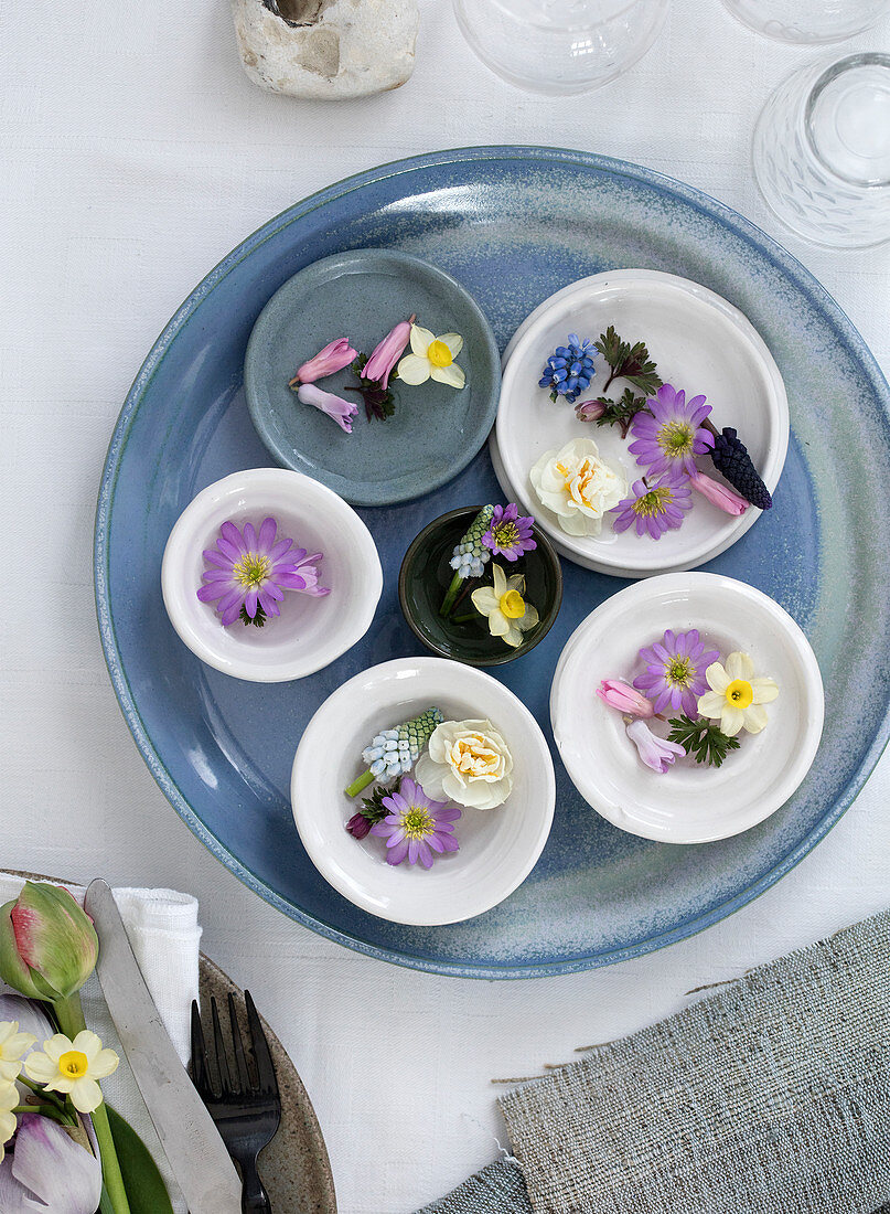 Various spring flowers in bowls on a blue plate