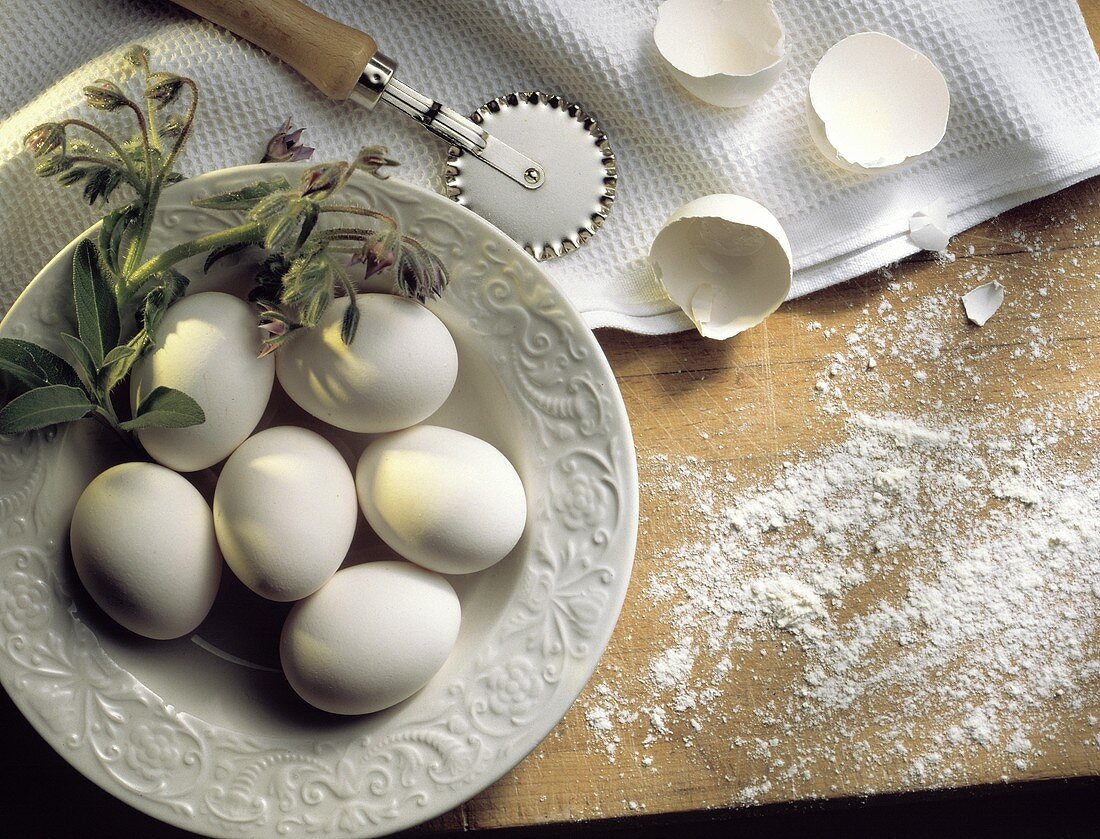 weiße Eier auf Teller, Deko: Borretsch, Teigrädchen, Mehl