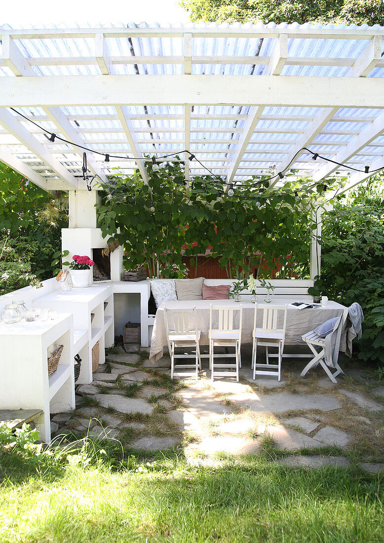 A dining table with chairs and a bench with green plants on a covered terrace