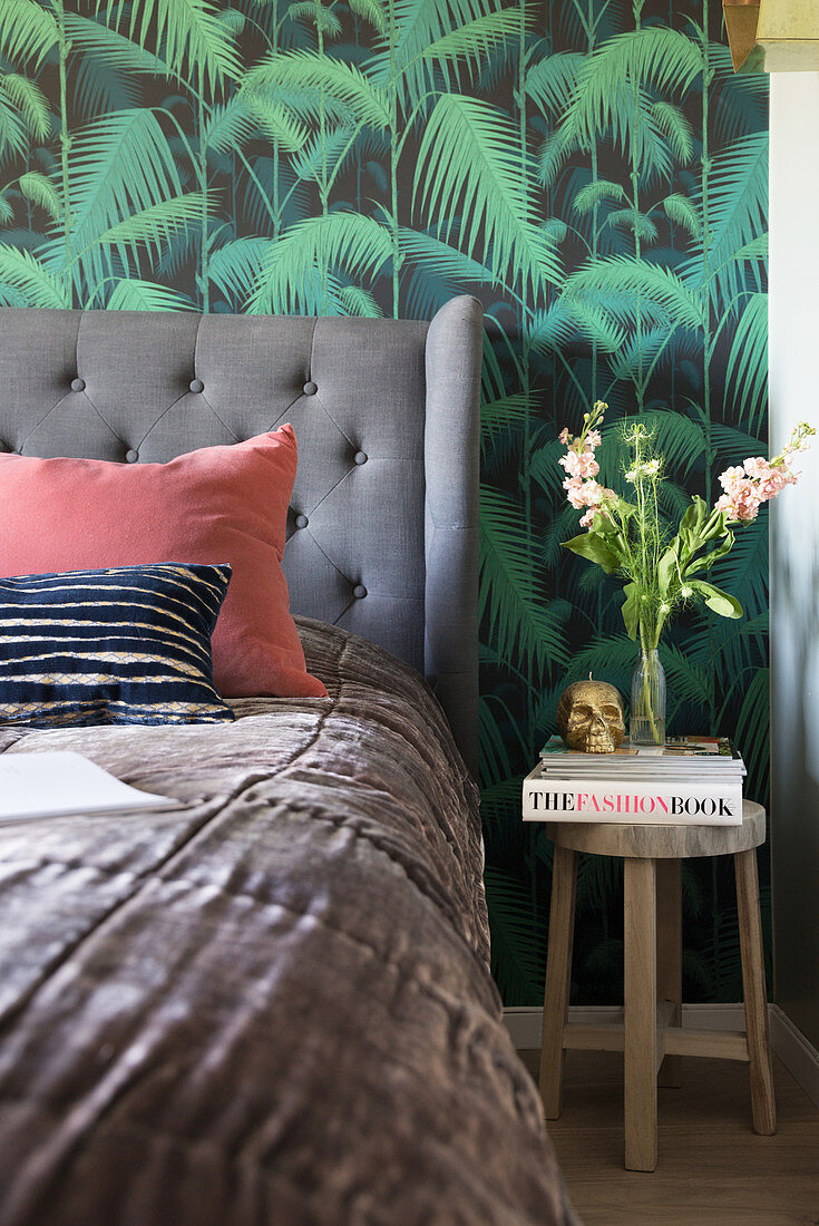 A bed with an upholstered headboard against jungle wallpaper