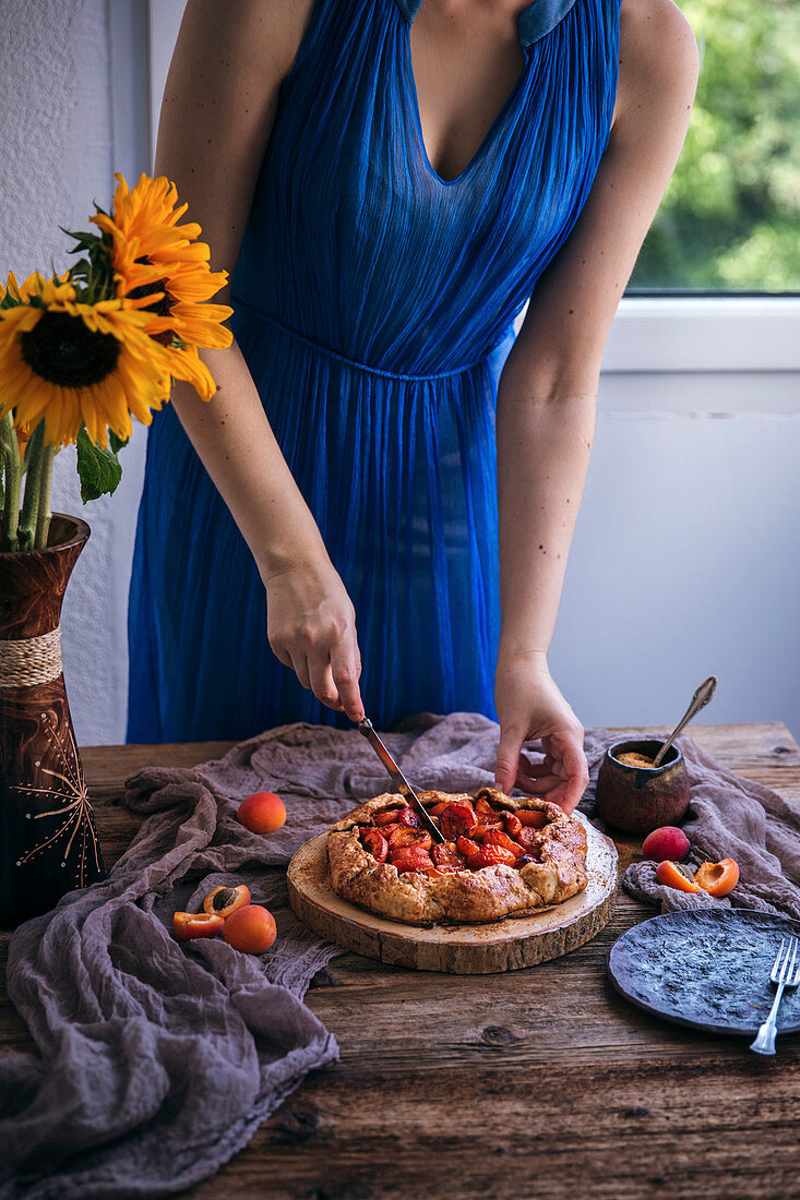 Frau im blauen Kleid schneidet Aprikosen-Galette an