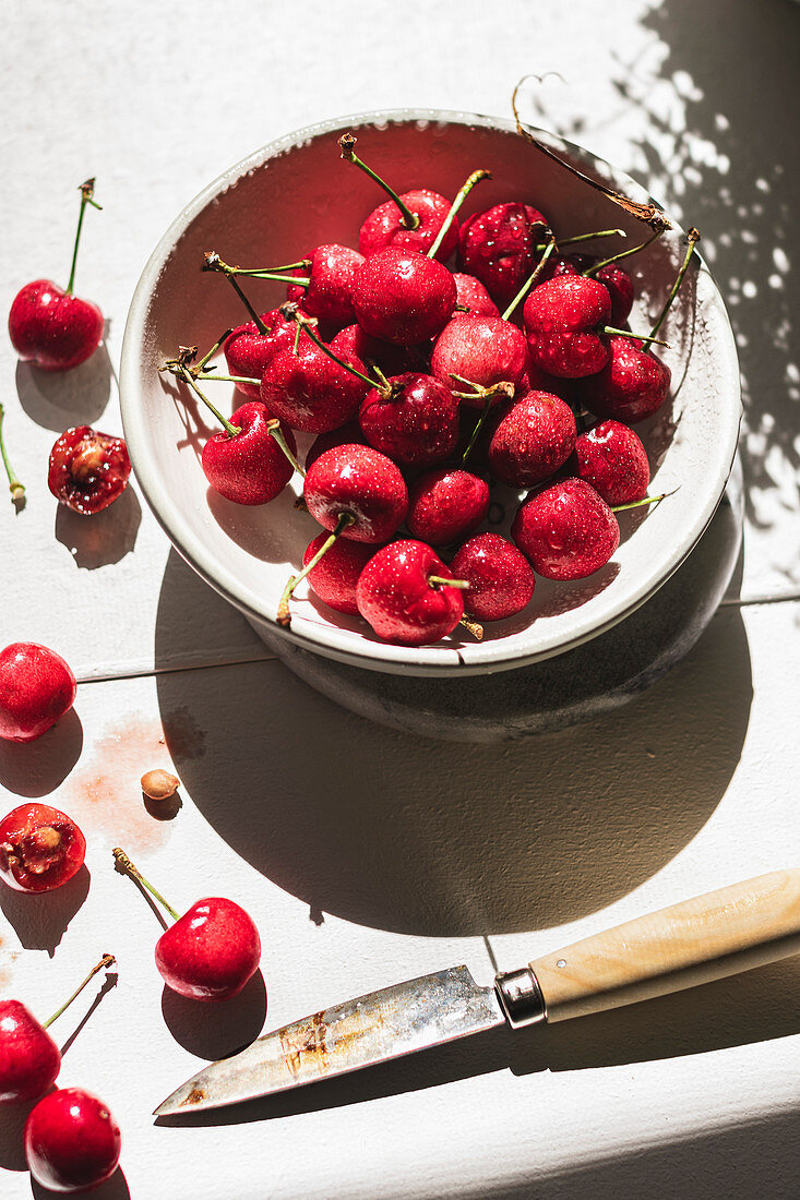 Cherries in a bowl and scattered on a white table