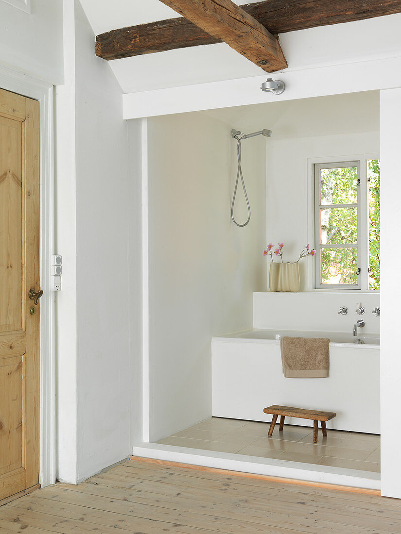 A view from a hallway with wooden beams into a small bathroom with a bathtub