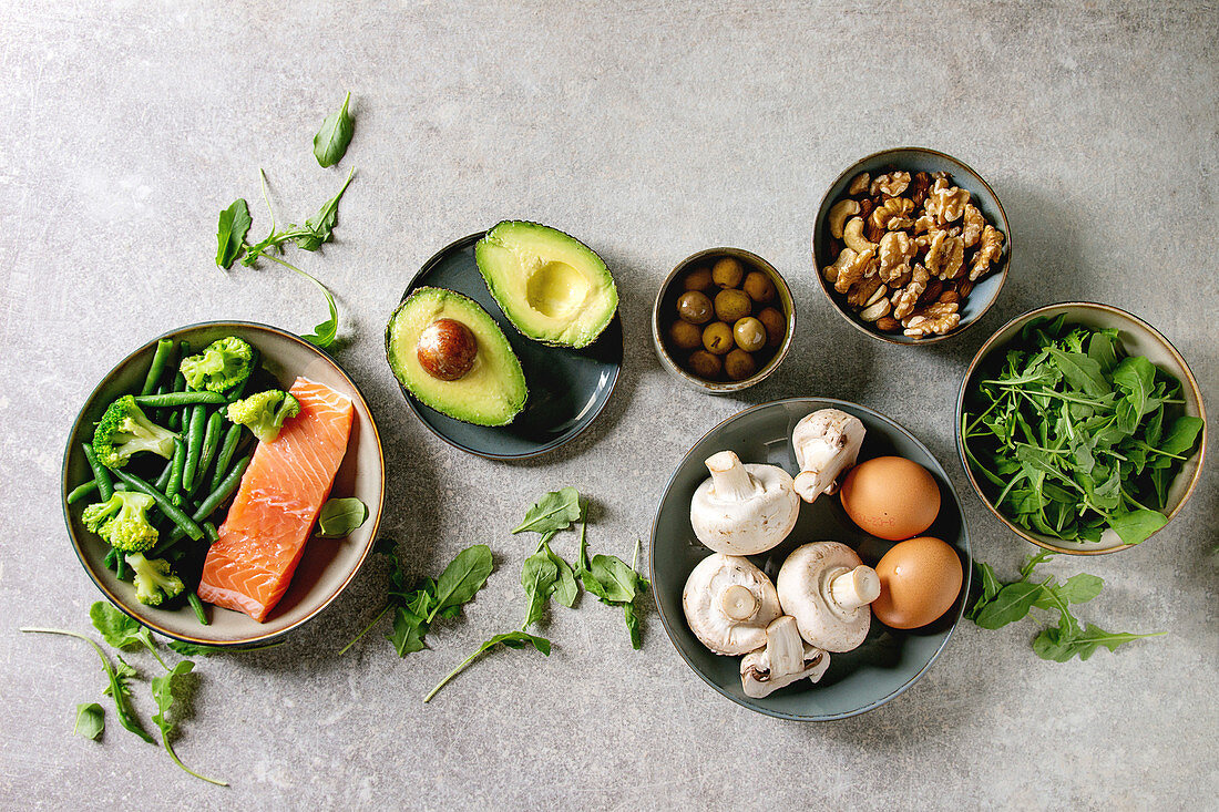 Ketogenic diet ingredients for cooking dinner. Raw salmon, avocado, broccoli, bean, olives, nuts mushrooms, eggs in ceramic bowls