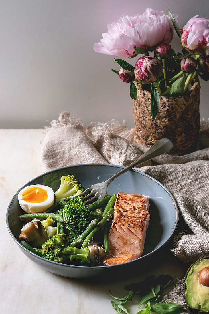 Ketogenic low carb diet dinner grilled salmon, avocado, broccoli, green bean and soft boiled egg in ceramic bowl