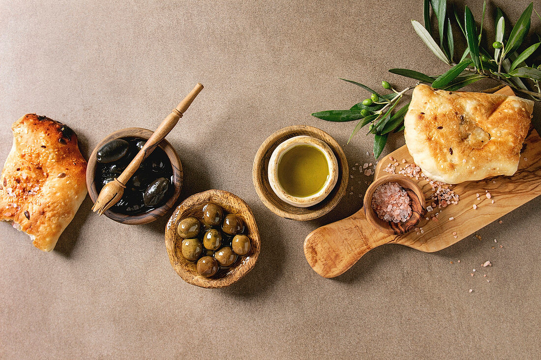 Variety of green and black whole olives in olive oil served in bowls with fresh baked ciabatta bread