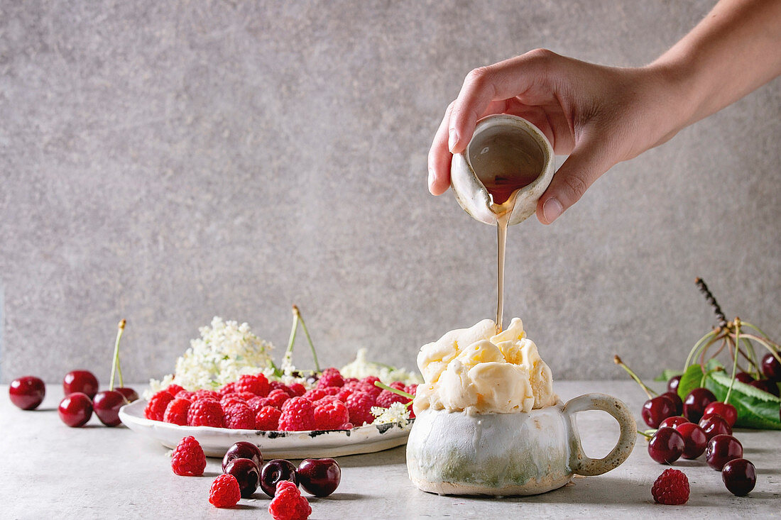 Homemade ricotta vanilla gelato ice cream served in ceramic mug with fresh raspberries, cherry berries, elderflowers