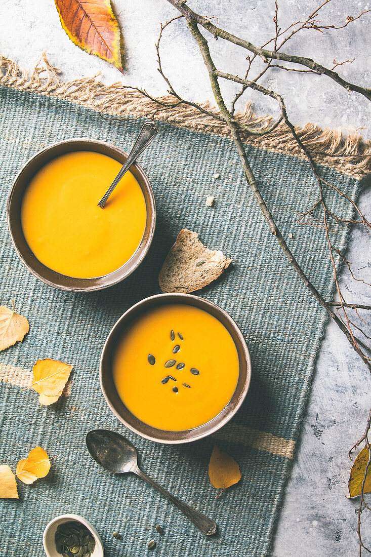 Homemade pumpkin soup in bowls and autumn leaves