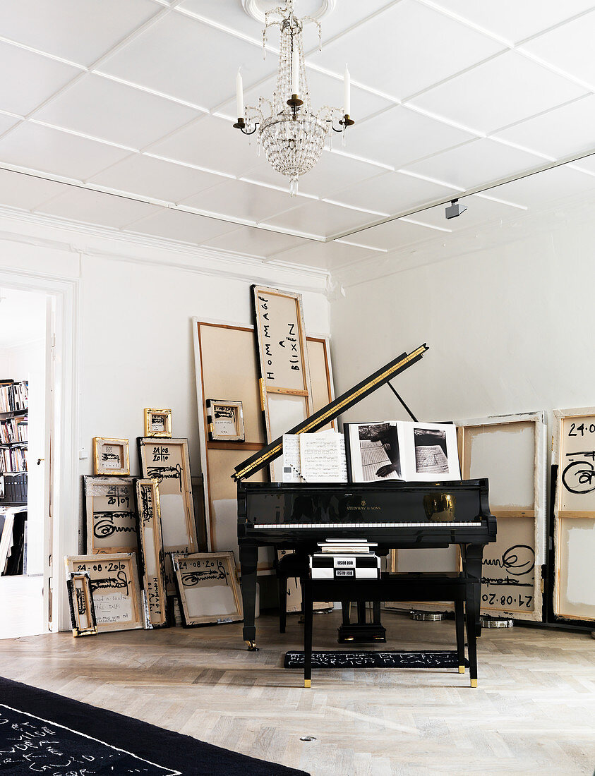 A grand piano in the corner on a room with painted canvases on the wall