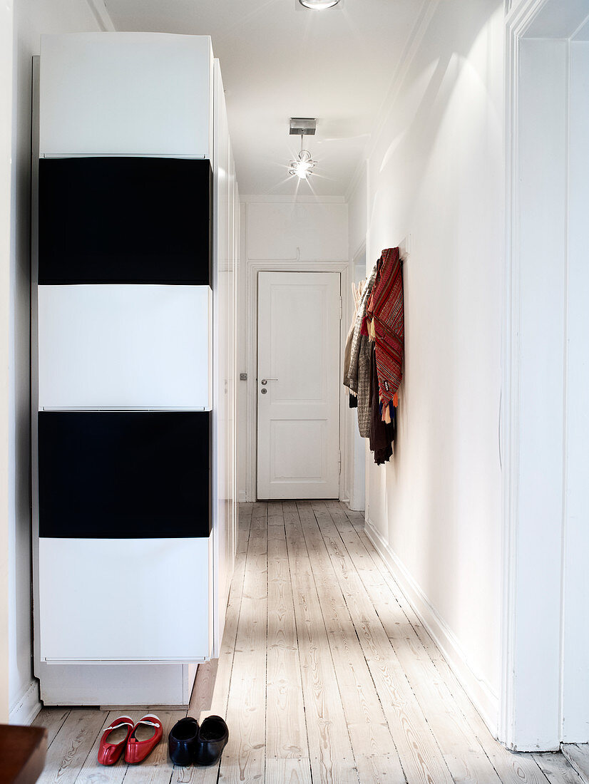 Black and white cupboard in the hallway with light wooden floorboards
