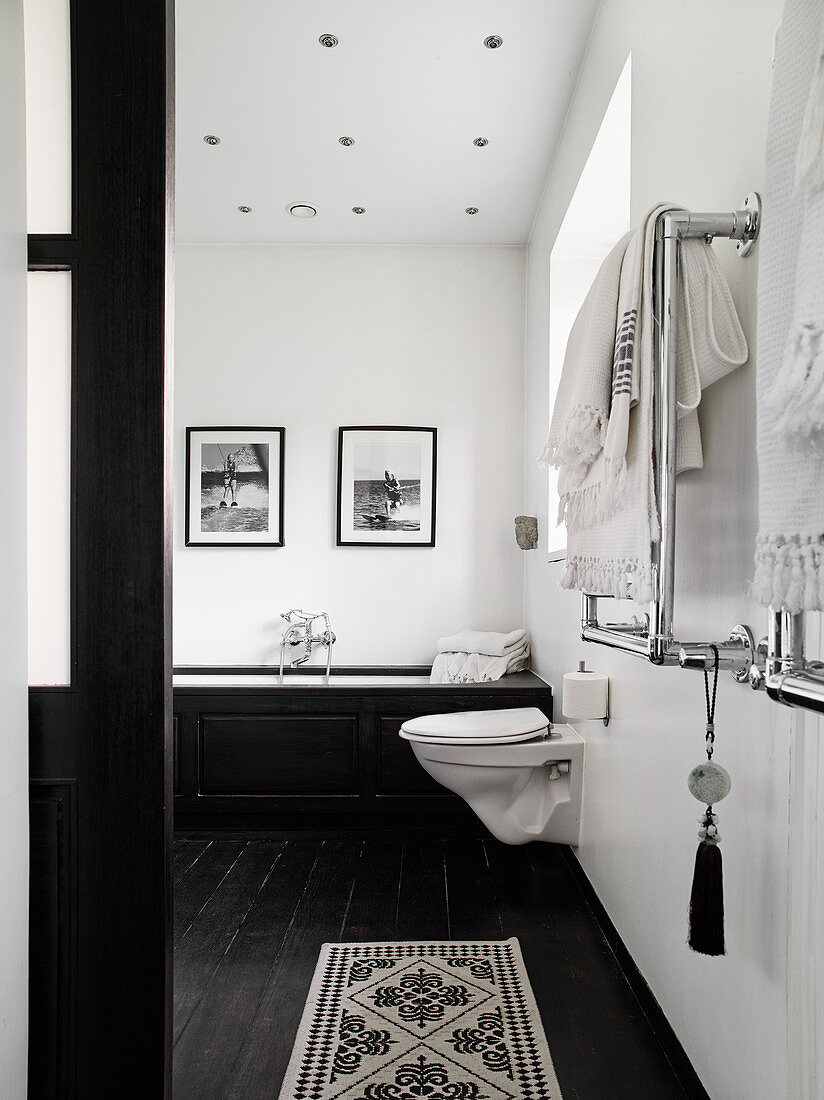 Toilet and bathtub in the bathroom with white walls and black painted wooden floor