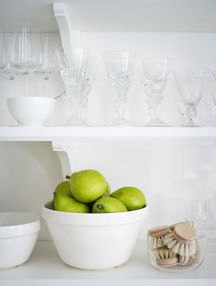 Green pears in a bowl on a kitchen shelf with glasses