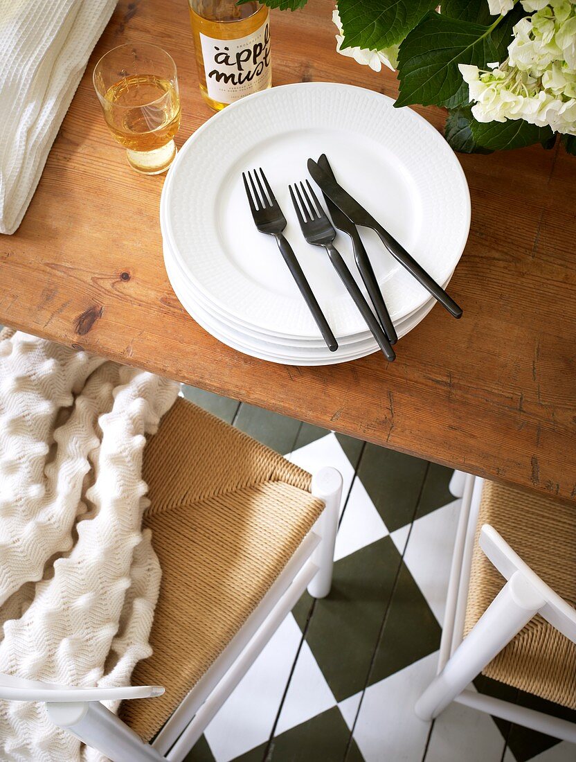 Black cutlery, a stack of plates, and apple juice on the wooden table