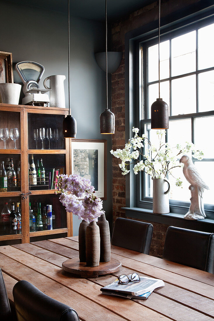 Wooden table with leather chairs, overhead pendant lights in front of the cupboard and window