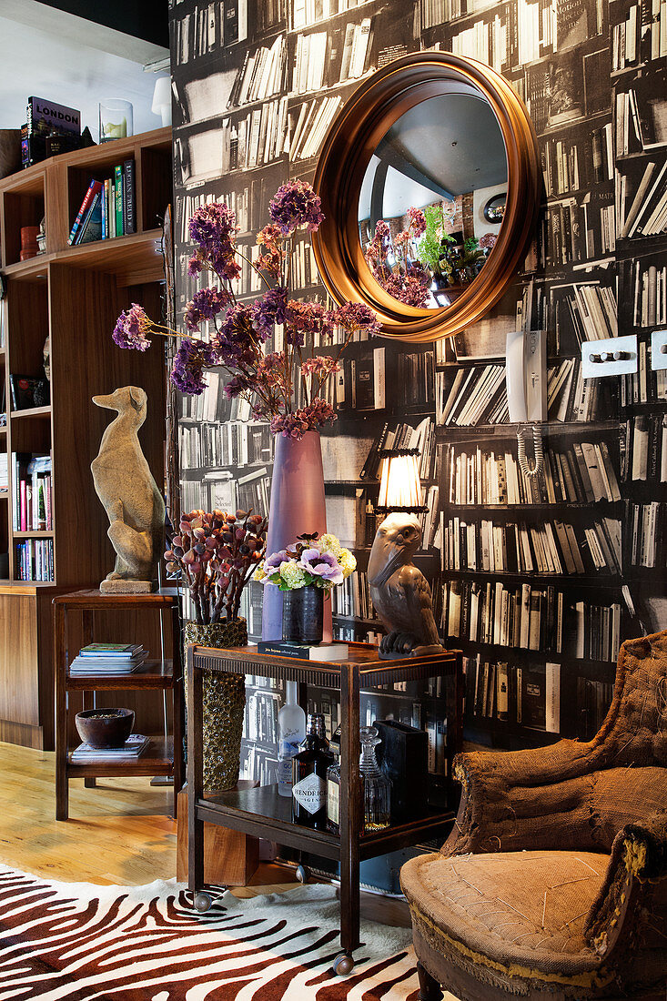 A bar cart with a vintage table lamp and an armchair in front of a bookcase