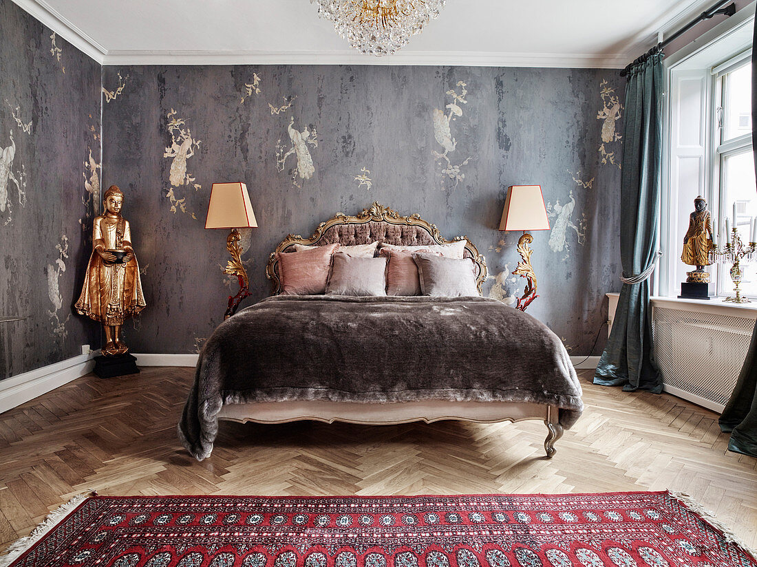 Doppelbett mit antikem Betthaupt, flankiert von Stehleuchten und goldfarbene Statue im Schlafzimmer