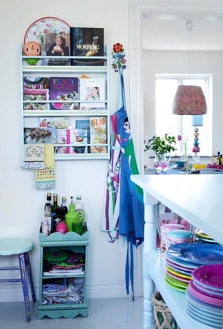 Plates on a shelf and a wall-mounted book rack with cookbooks, including a shelf with a trivet in the open plan kitchen-living room