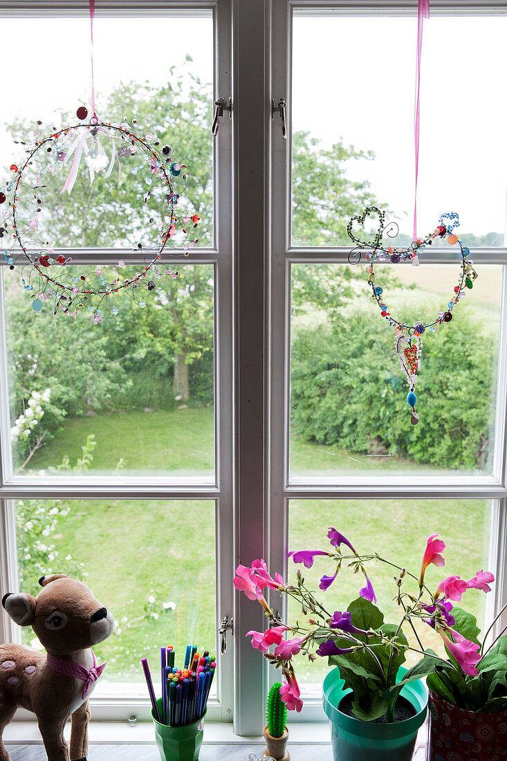 Window decoration with beads, indoor flowers, a pencil holder and a plush Bambi on a windowsill
