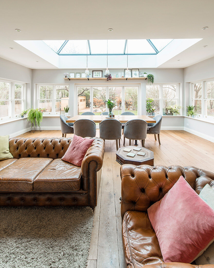 Chesterfield sofa and dining table below skylight in open-plan interior
