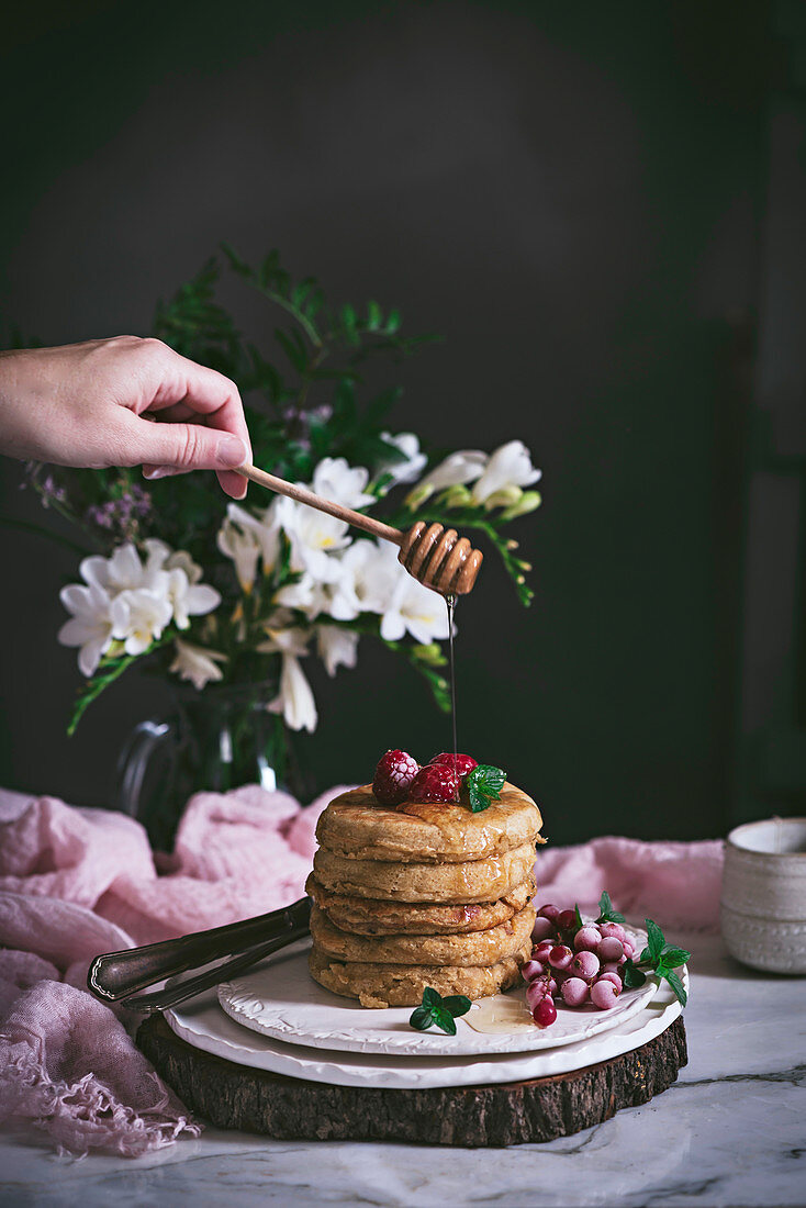 Gestapelte Himbeer-Pancakes mit Honig beträufeln