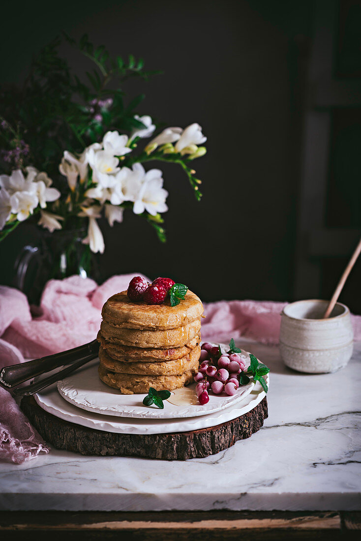 Stack of raspberry pancakes with fresh berry on porcelain plate at marble tabletop text to case with flowers over dark background