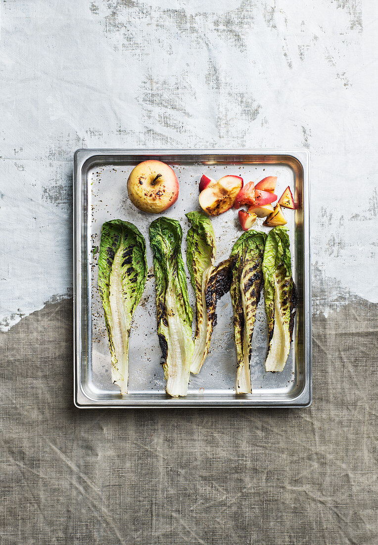 Grilled salad leaves and apples on a baking sheet