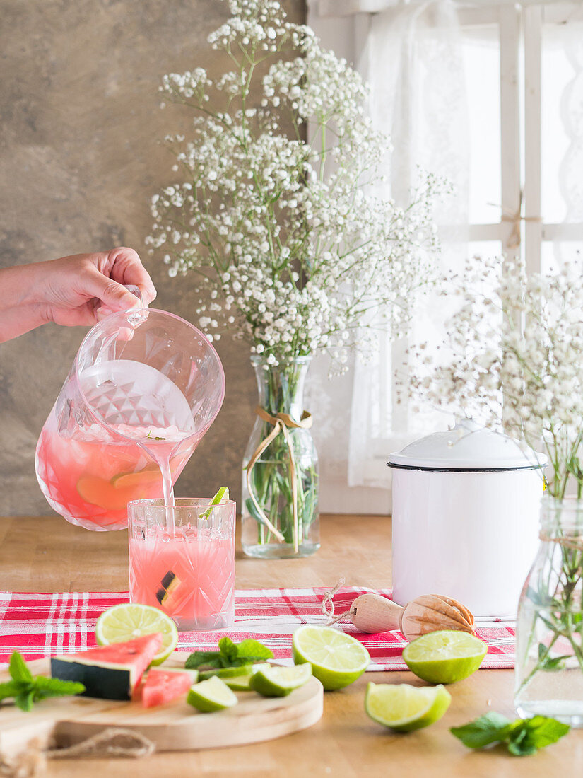Rosa Limonade mit Wassermelonen- und Limettenscheiben in Glas einschenken