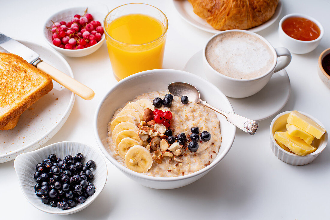Breakfast with oatmeal with berries and nuts, croissants, toasts with jam and butter, coffee and orange juice