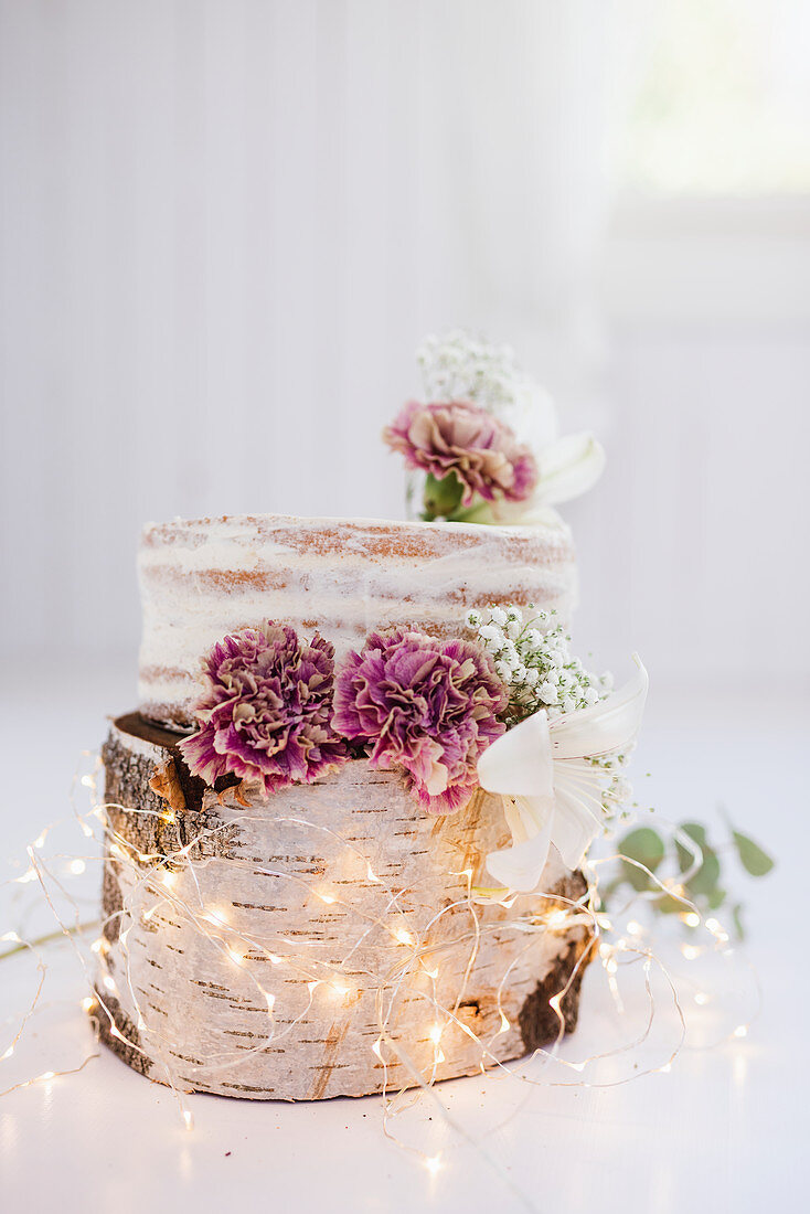 A naked cake on a tree stump with a chain of fairy lights