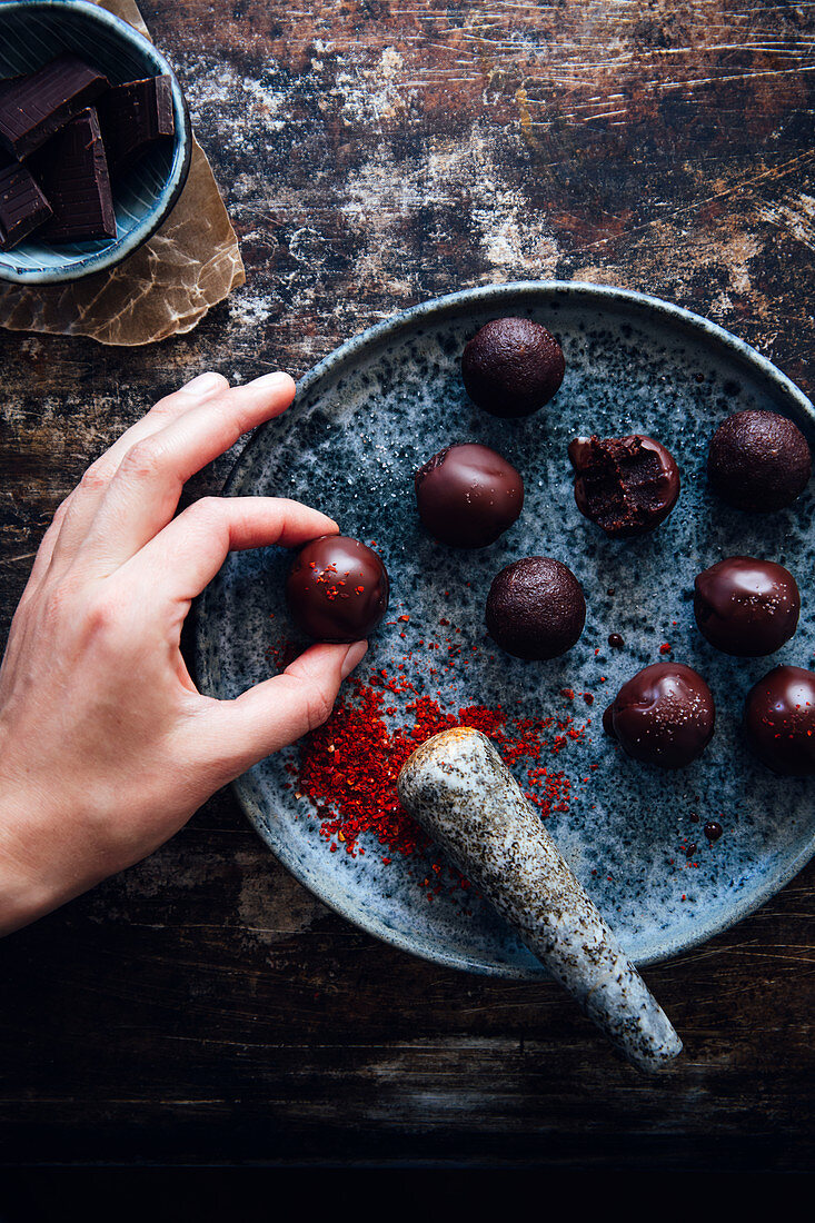 A hand taking a chocolate truffle with chilli powder
