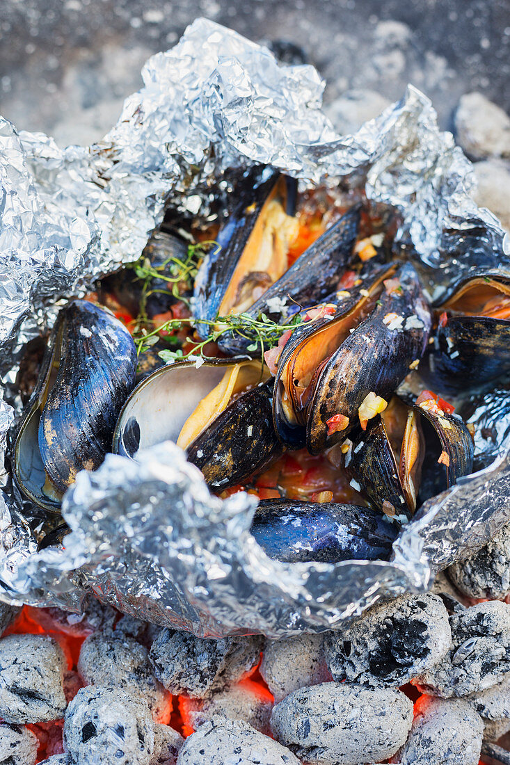 Grilled mussels in aluminium foil on glowing coals