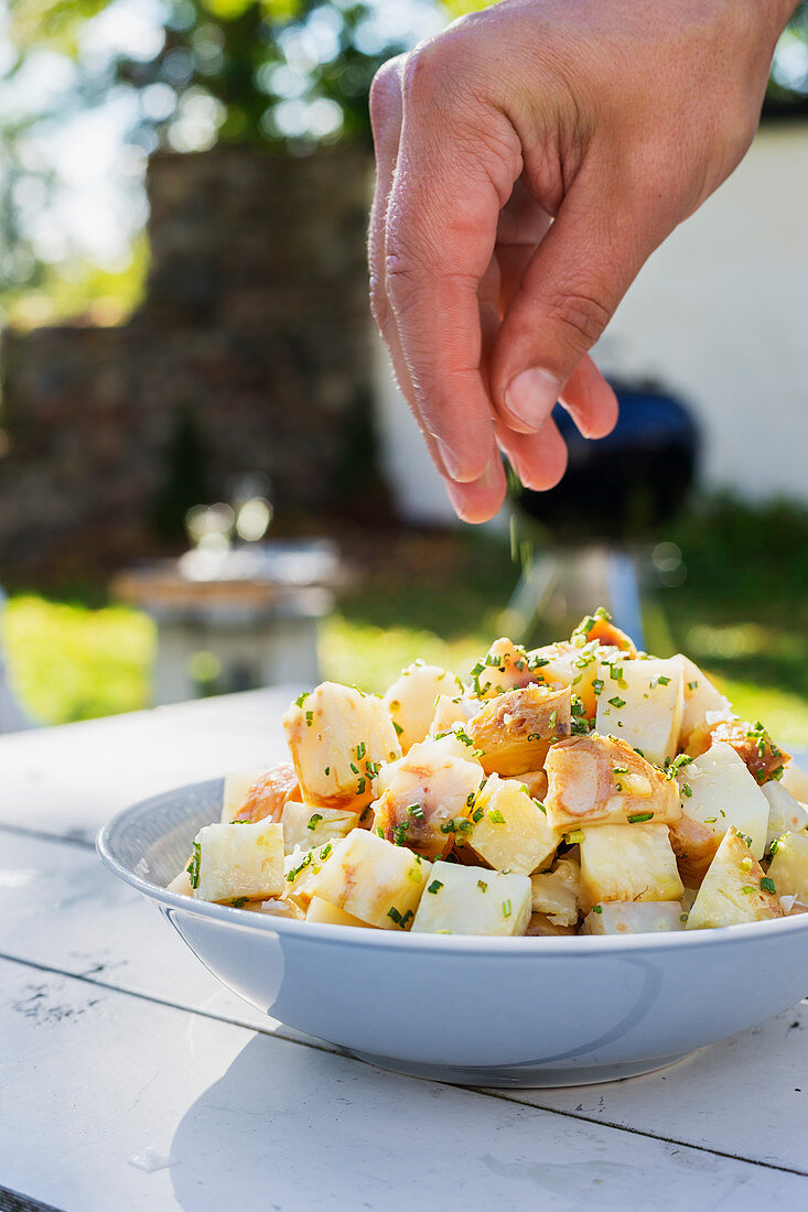 Salat auf Tisch im sommerlichen Garten wird mit Salz bestreut