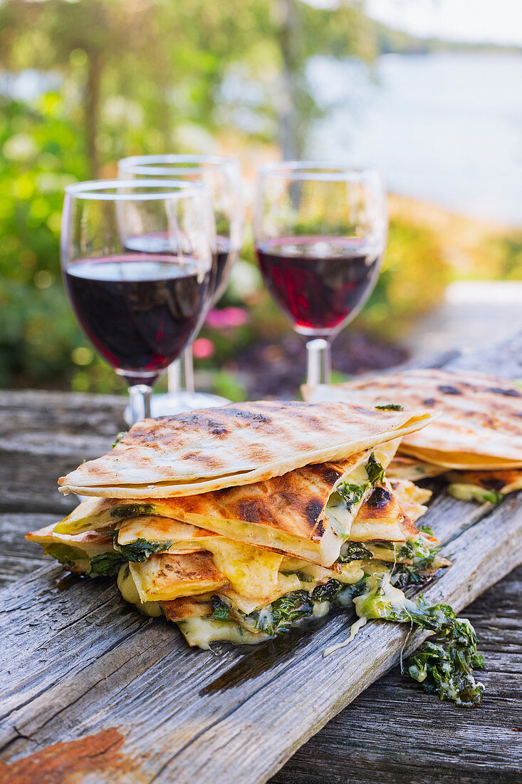 Panini with spinach and cheese served with red wine outside on a wooden surface
