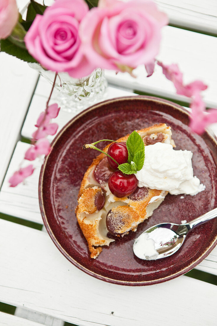 A slice of cherry pie with cream on a wooden table