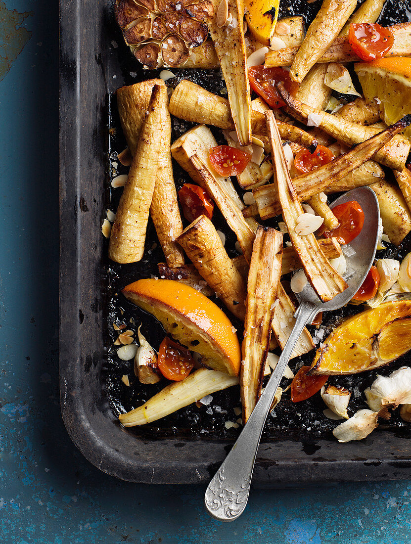 Oven-roasted vegetables with garlic and oranges on a baking tray