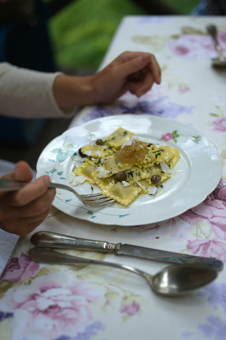 Frau isst Artischockenravioli mit karamellisierten Zwiebeln und Oliven