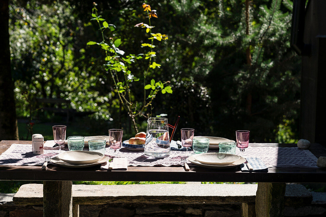 Gedeckter Gartentisch mit bunten Gläsern und Wasserkaraffe