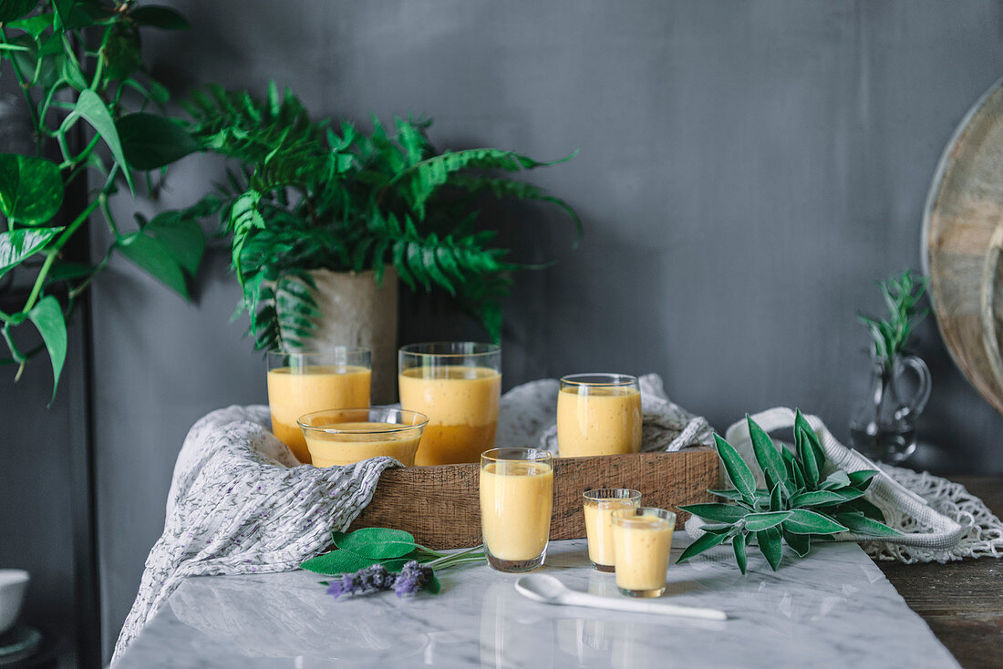 Tasty aromatic mango mousse in glass mugs and spoon on table decorated with green plants