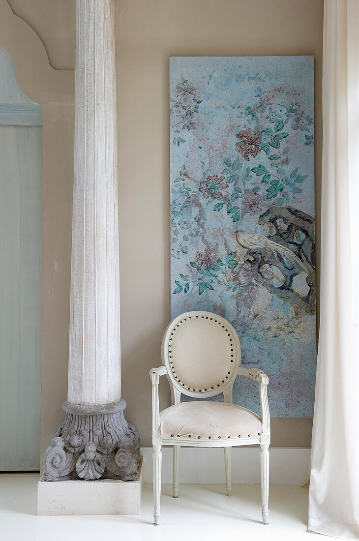 White Baroque chair next to antique pillar and in front of pale blue artwork