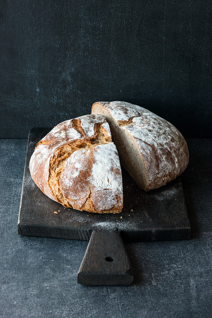 A loaf of country bread: classic sour dough bread, halved on a wooden board