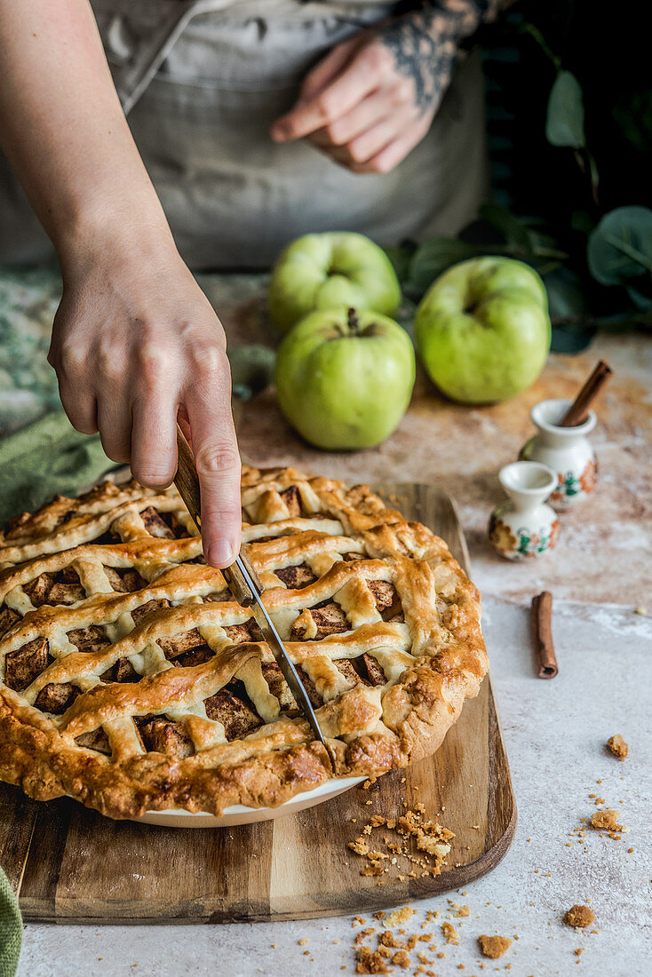 Person cuts freshly baked apple pie with cinnamon