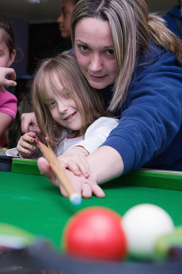 Adult teaching a child to play pool
