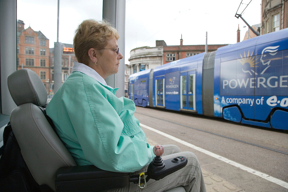Woman wheelchair user waiting by a shelter at tram stop